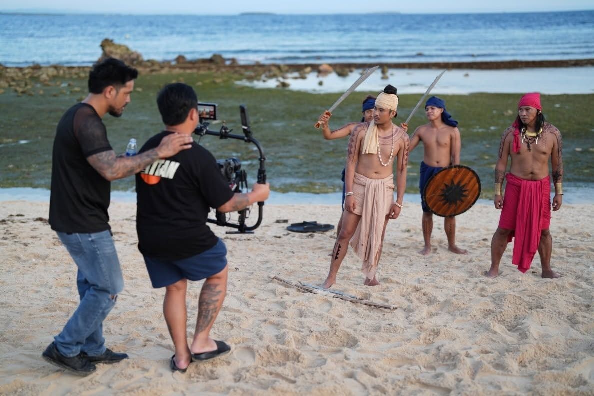 A camera operator with a gimbal films warriors on the beach
