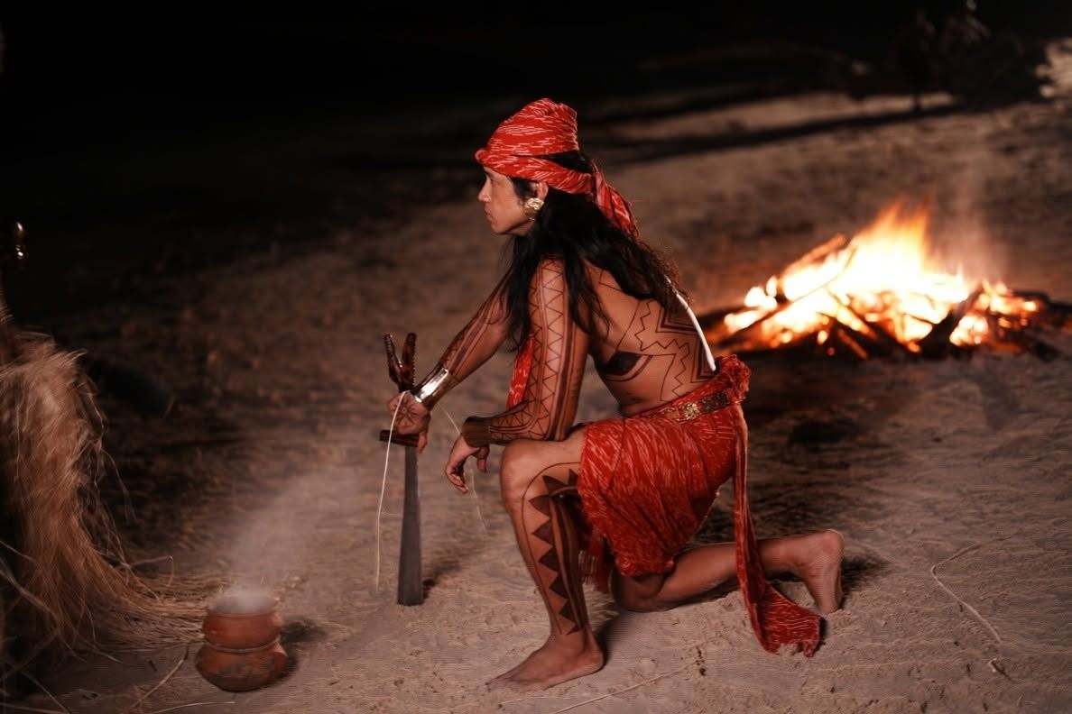A warrior kneels by a fire at night with a blade