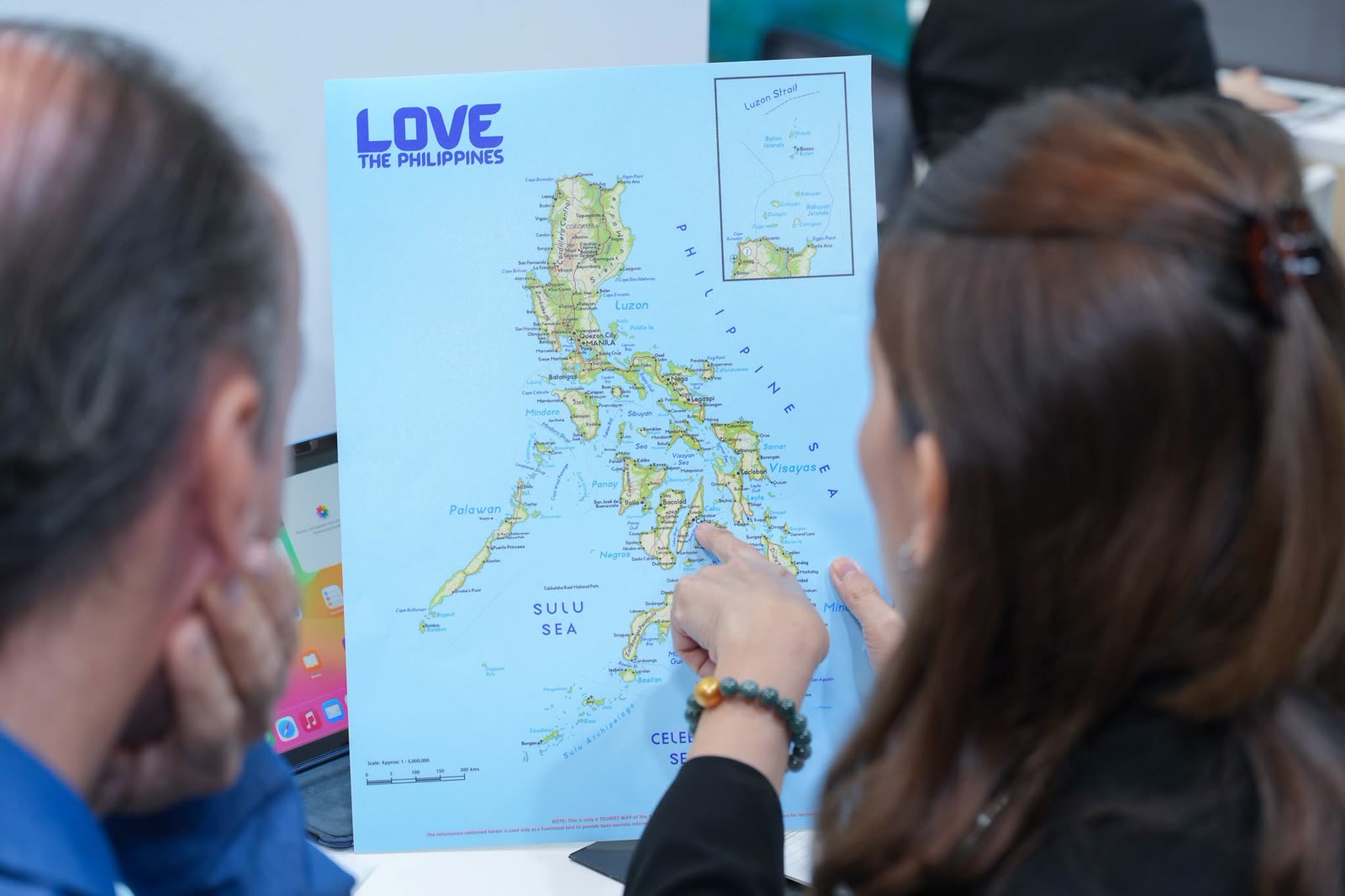 An exhibitor points to a place on a LOVE the Philippines map for a buyer