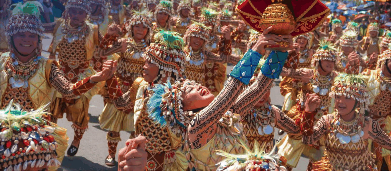 Sinulog street dancers in shell-adorned costumes, one raising a Santo Niño image
