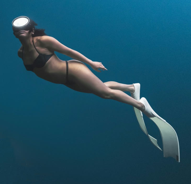 Reference photo of a freediver in a black bikini and white long bi-fins swimming in blue water