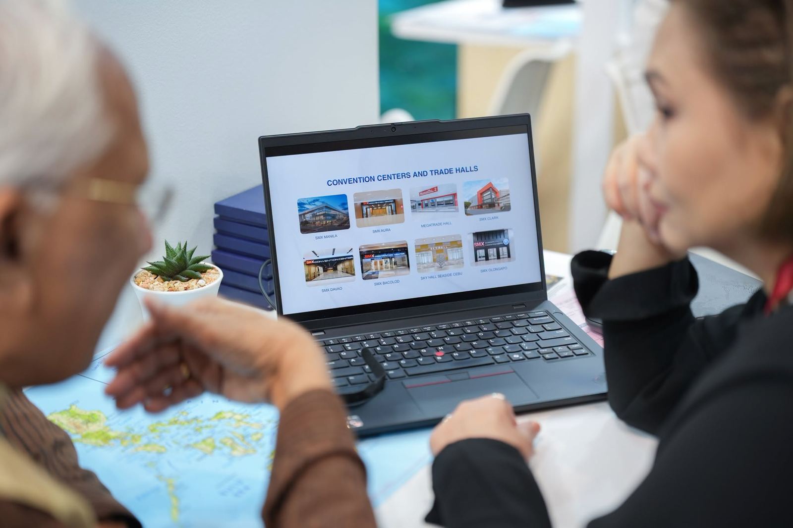 A laptop on a meeting table shows a slide titled Convention Centers and Trade Halls