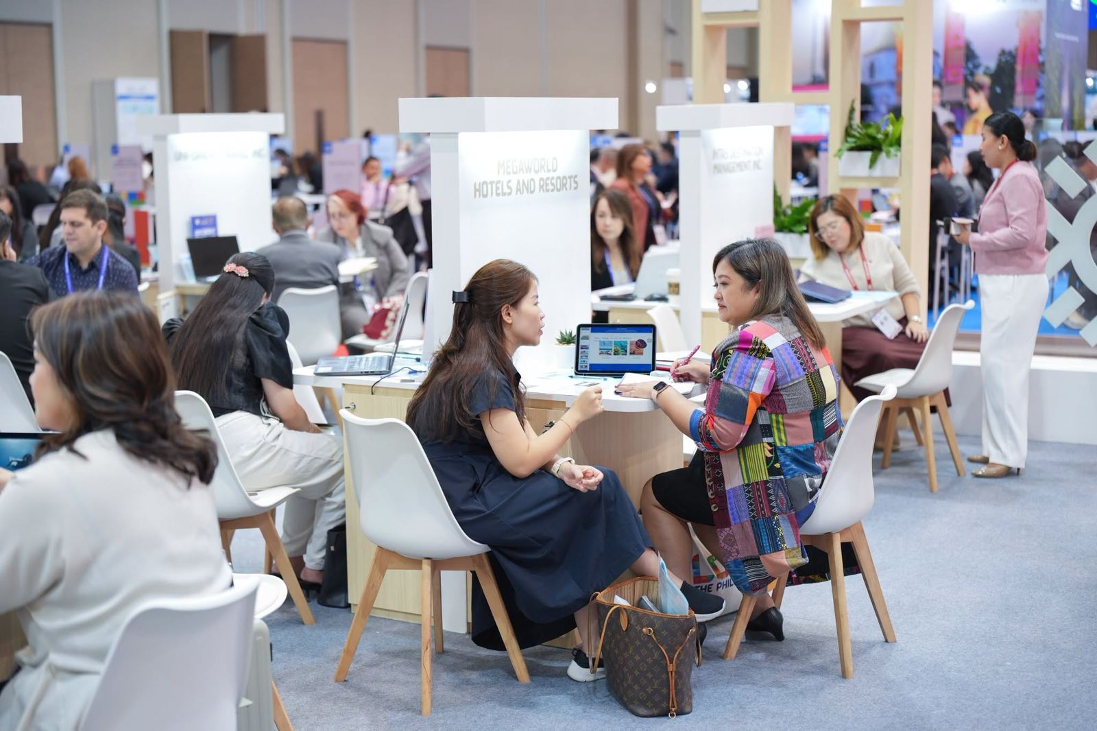 Buyer meetings at the white tables of the pavilion, a Megaworld Hotels and Resorts sign behind